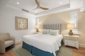 A bedroom with a bed, a chair, a ceiling fan, and a wall-mounted picture.