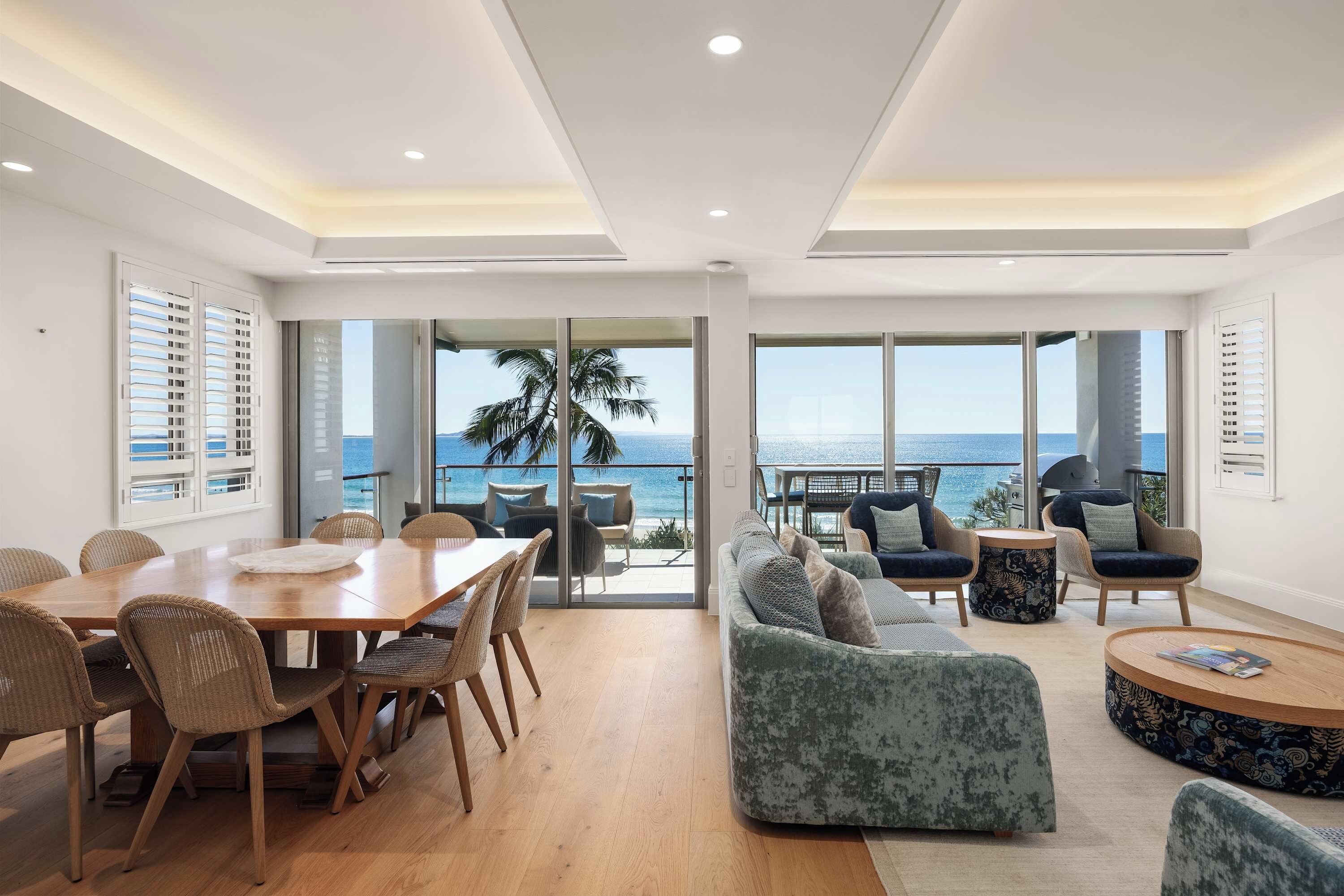 A modern living room with a dining area, large windows, and a view of the ocean.