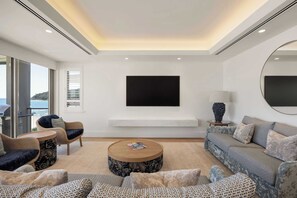 Een moderne woonkamer met een grote flatscreen televisie aan de muur, een ronde salontafel en comfortabele zitplaatsen, inclusief een bank en fauteuils.