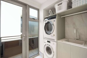 Een wasruimte met een voorlader wasmachine en droger, een wasbak en een raam.