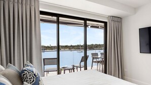 Une chambre d’hôtel dotée d’un grand lit, offrant une vue sur le port de plaisance, et comprenant un coin repas avec des sièges à l’extérieur.