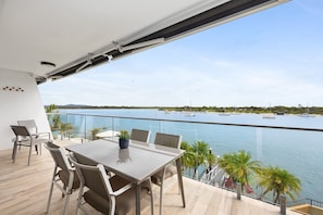 Un balcon avec une table et des chaises, donnant sur une étendue d’eau calme où naviguent des bateaux.