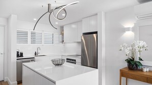 Une cuisine moderne dotée d’un îlot central, d’appareils électroménagers en acier inoxydable et d’un luminaire au plafond au design original.