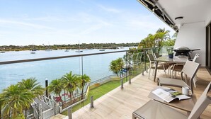 Un balcon avec vue sur l’eau, une table avec des chaises et un barbecue.