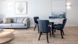 Un salon moderne avec un canapé gris, une table de salle à manger ronde entourée de chaises et des œuvres d’art accrochées aux murs.