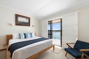 Relax in a serene space with a large bed, wooden headboard, and a view of the water through a sliding glass door.