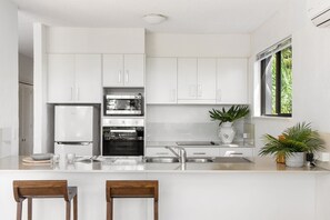 A modern kitchen with white cabinetry, a built-in oven, a microwave, and a large window providing natural light.