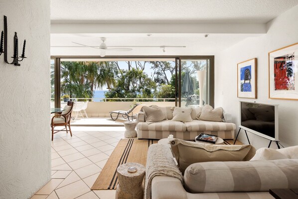 A modern living room with a large window, a ceiling fan, and a flat-screen TV.