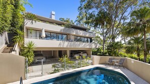 Una casa moderna de dos pisos con piscina, mobiliario exterior y exuberante follaje.