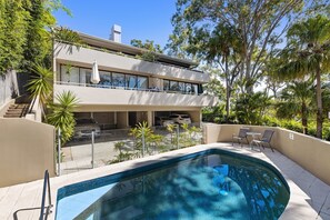 A modern two-story house with a swimming pool, outdoor seating, and lush greenery.