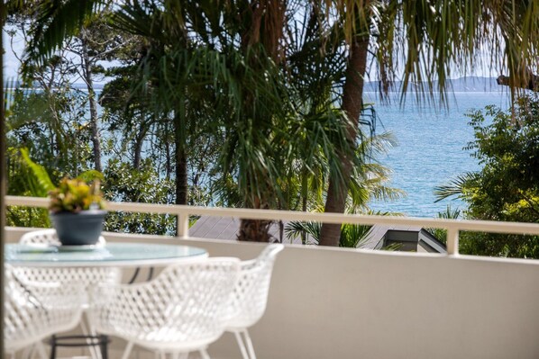 A balcony with a view of the sea, white wicker furniture, and a potted plant.