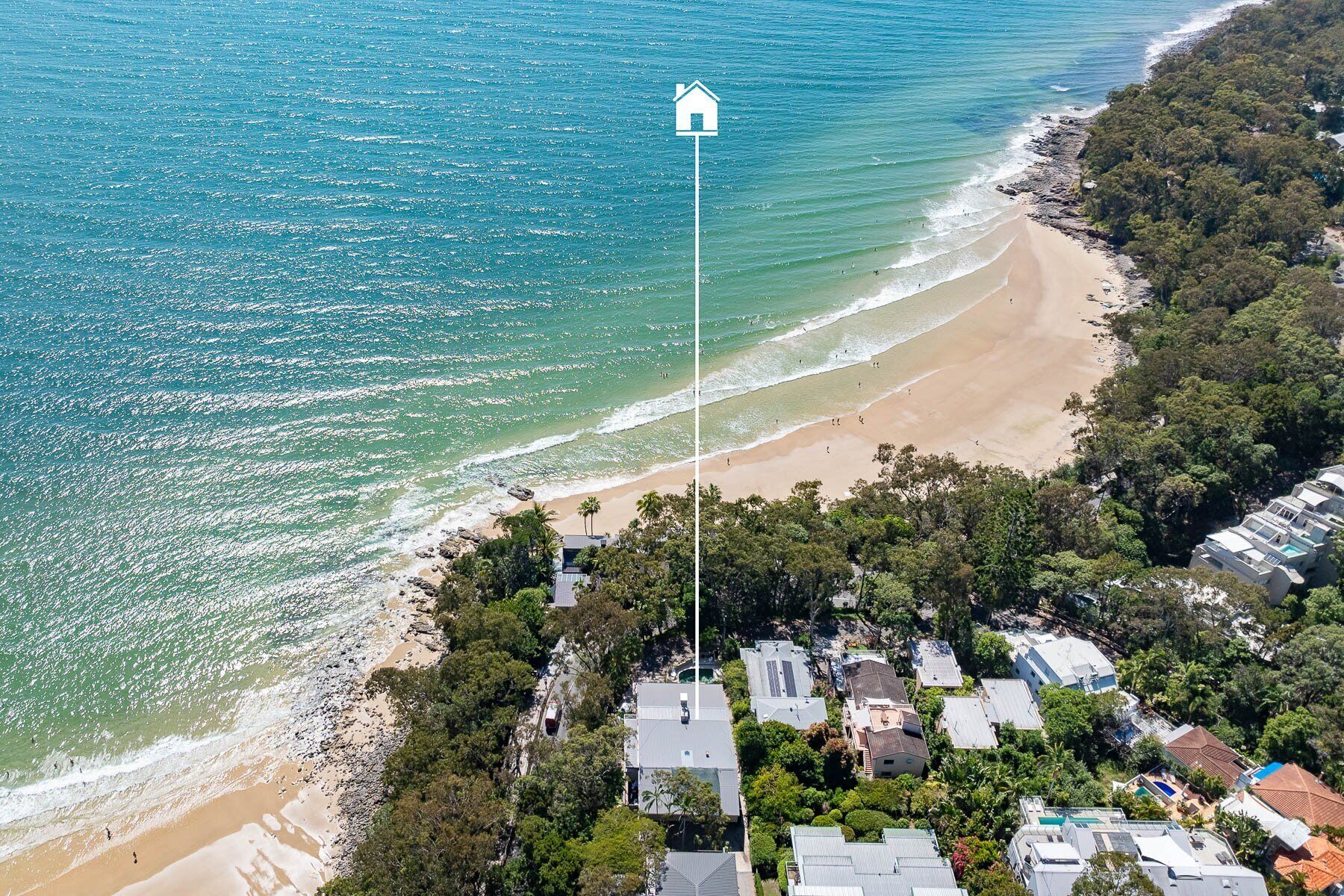 An aerial view of a coastal area with a beach, houses, and a flagpole with a house symbol.