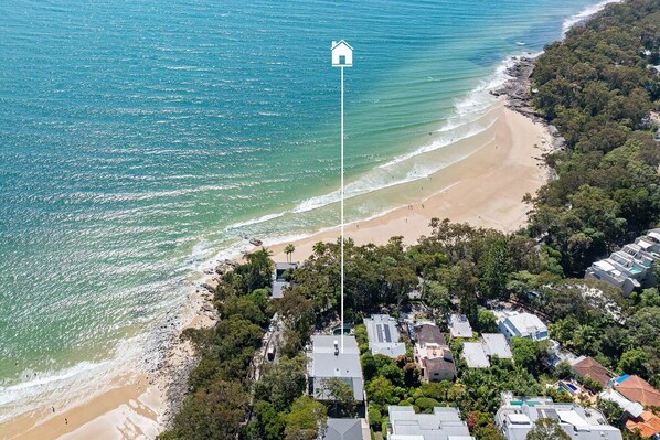 An aerial view of a coastal area with a beach, houses, and a flagpole with a house symbol.