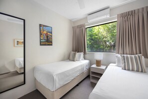 Ein Hotelzimmer mit zwei Einzelbetten, einem Fenster mit Vorhängen, einer Wandklimaanlage und einem Poster von Australien.