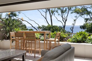 An outdoor seating area with a table and chairs, overlooking a body of water and trees. - Cove Point 5 - Stylish Cove Escape (Noosa Heads)