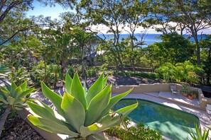 Ein Poolbereich mit Blick auf das Meer, umgeben von üppiger Vegetation und Bäumen.