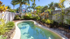 Une piscine entourée de plantes tropicales et délimitée par une clôture en bois.