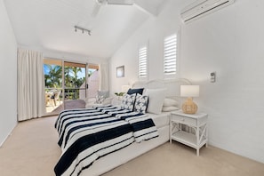 A bedroom with a large bed, a nightstand, a lamp, and a view of the outdoors. - Modern Noosa Retreat - Private Pool (Noosa Heads)