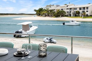 A dining area with a view of the beach and boats, featuring a table with chairs and a decorative lantern.