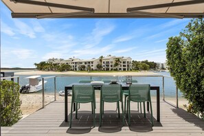 Een terras met tafel en stoelen met uitzicht op een strand en een complex van gebouwen.