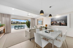 A modern living room with a glass dining table, a sofa, and a view of a water body outside. - Driftwood 2 - Riverfront with Jetty (Noosaville)