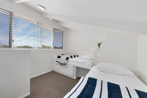 Een slaapkamer met een stapelbed, een nachtkastje, een raam met zonwering en uitzicht op buiten.