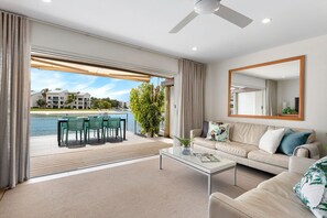 Relax in this stylish living room with a view of the water and cityscape, featuring a comfortable sofa, dining area, and large mirror.