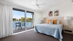 A hotel room with a bed, two bedside lamps, a ceiling fan, and a view of a body of water through a sliding glass door.