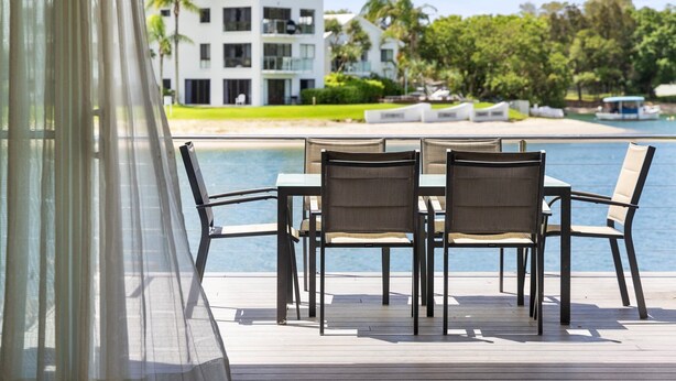 A deck with a table and chairs overlooking a pool, with a building in the background.