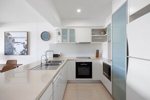 A modern kitchen with white cabinetry, a stainless steel sink, a built-in oven, and a refrigerator.