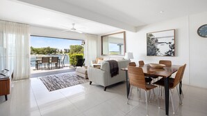 A modern living room with a dining area, a large window offering a view of the outdoors, and a ceiling fan.