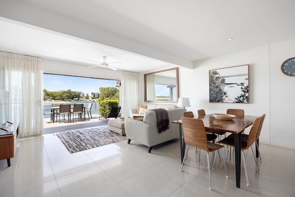 A modern living room with a dining area, a large window offering a view of the outdoors, and a ceiling fan.