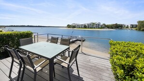 A deck with a table and chairs overlooking a lake, with buildings in the background.
