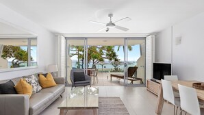 Una sala moderna con sofá, mesa de centro y televisor, que da a un balcón con vistas al mar.