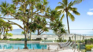 Zona de piscina con vista al océano, rodeada de palmeras y sillas de descanso.