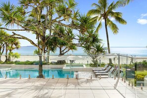 A pool area with a view of the ocean, surrounded by palm trees and lounge chairs.