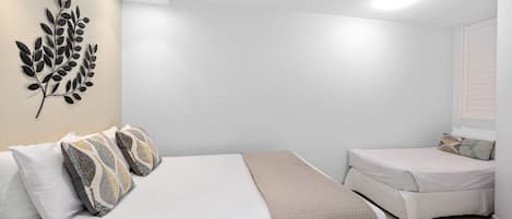 A hotel room with a bed, a bedside table, a wall-mounted decorative leaf art piece, and a window with blinds.