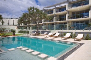 Um hotel moderno com piscina, espreguiçadeiras e um edifício de vários andares com varandas.