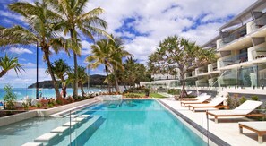 A swimming pool with lounge chairs, palm trees, and a modern building with balconies. - Fairshore 15 - Noosa Main Beach Stay (Noosa Heads)