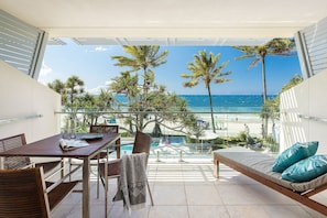 Un balcon avec vue sur la plage, une table avec des chaises et un canapé avec des coussins.