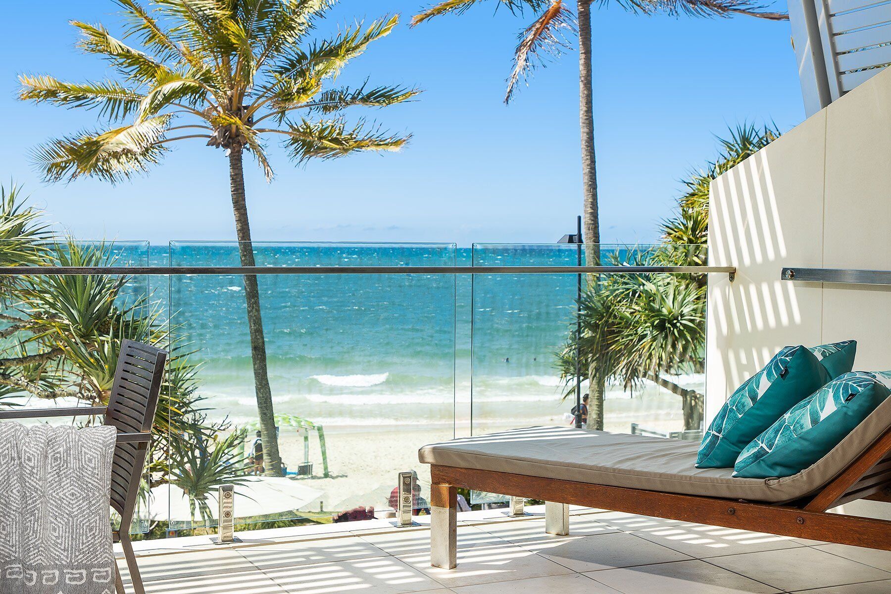 A balcony with a view of the ocean, a lounge chair with cushions, and a glass railing.