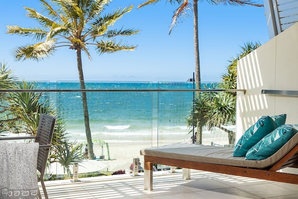 Un balcon avec vue sur l’océan, un fauteuil de relaxation avec des coussins et une rambarde en verre.