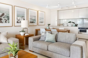 A modern living room with a grey sofa, a wooden coffee table, and a dining area with a white table and chairs.
