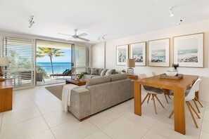 A modern living room with a large sofa, a dining table with chairs, and a view of the ocean through large windows. - Fairshore 22 - Main Beach Views (Noosa Heads)
