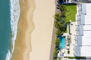 Um hotel à beira-mar com piscina, palmeiras e uma praia de areia.