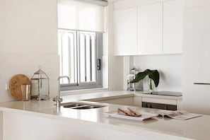 A modern kitchen with a large window, a sink, a stove, and a countertop with a cutting board and a lantern.