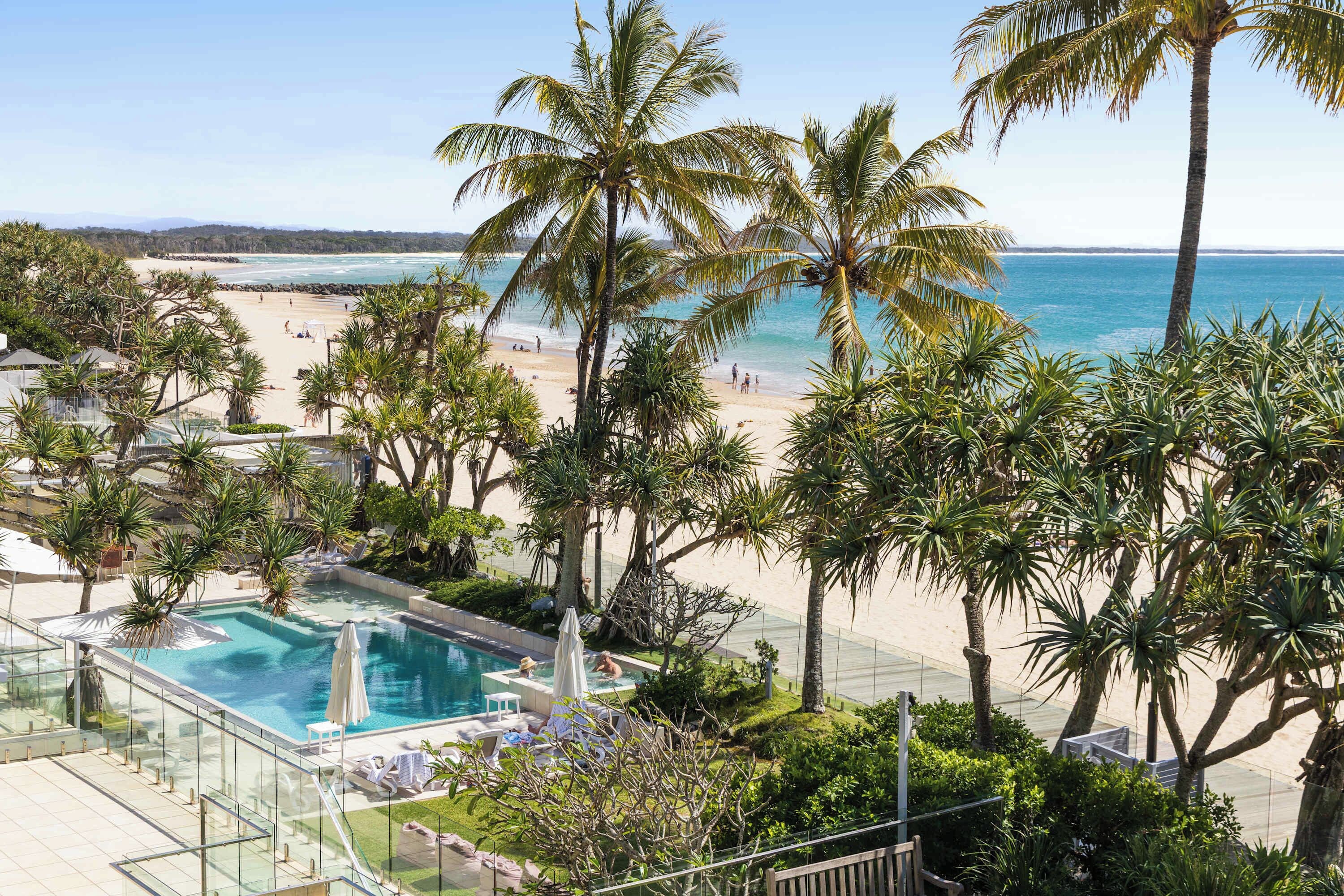 A resort with a pool, beach, and palm trees.