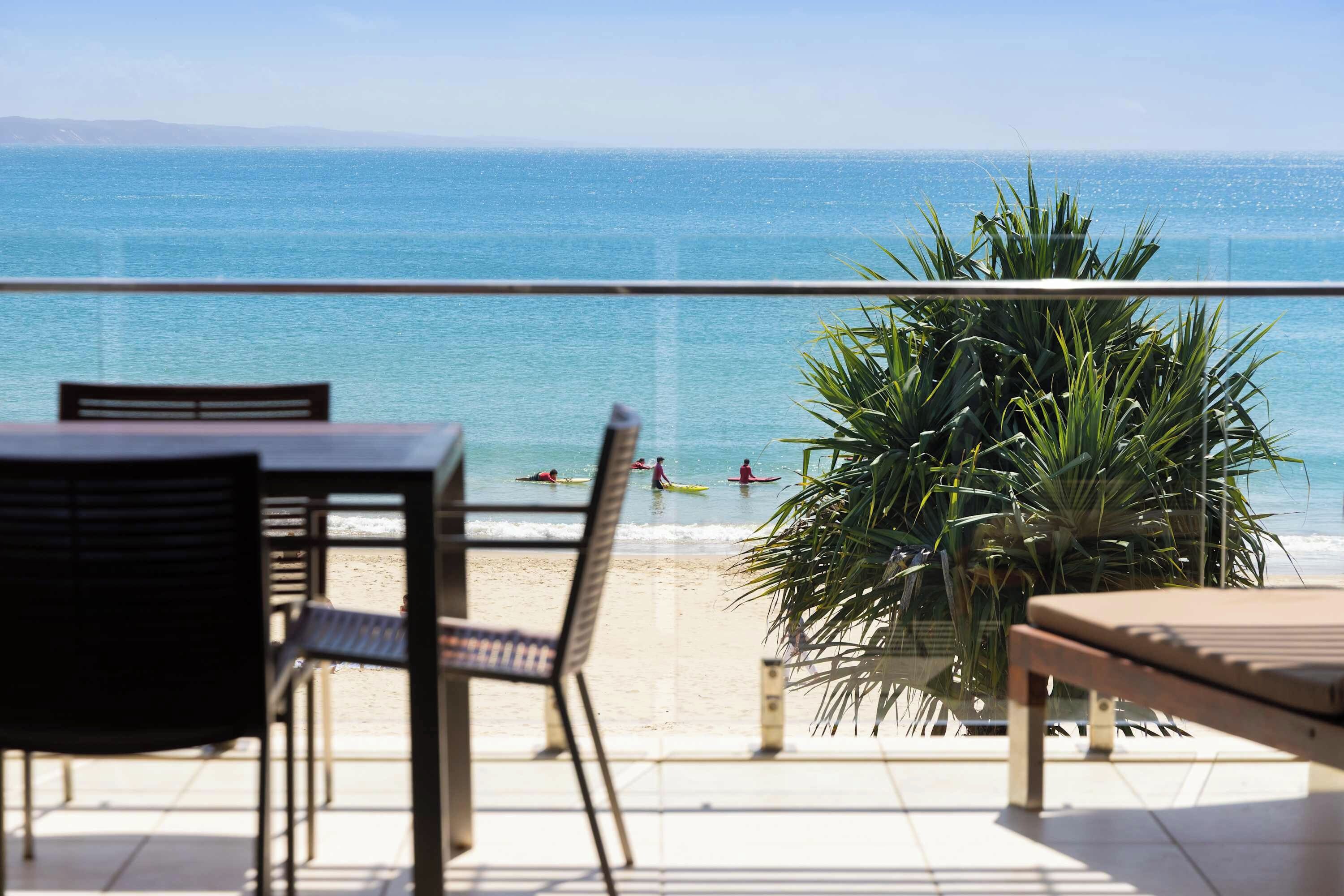 A terrace with a view of the beach and ocean, featuring a table and chairs, and a potted plant.