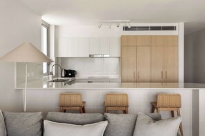 A modern kitchen with white cabinetry, a central island, and a dining area with wicker chairs.