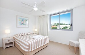 A bedroom with a bed, a nightstand, a chair, a window with a view, and a ceiling fan.